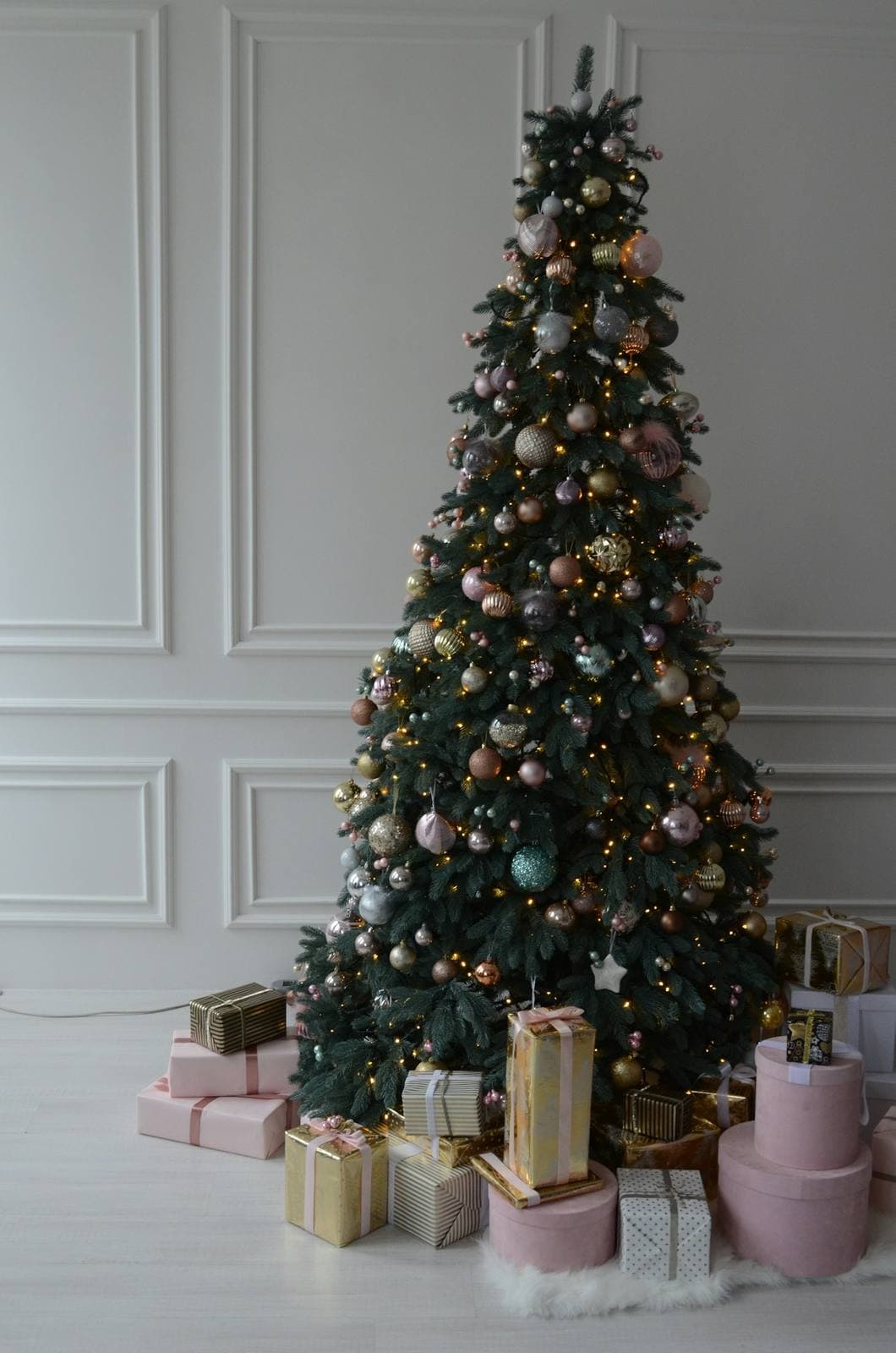 Geschmückter Weihnachtsbaum mit Geschenken vor heller Wand